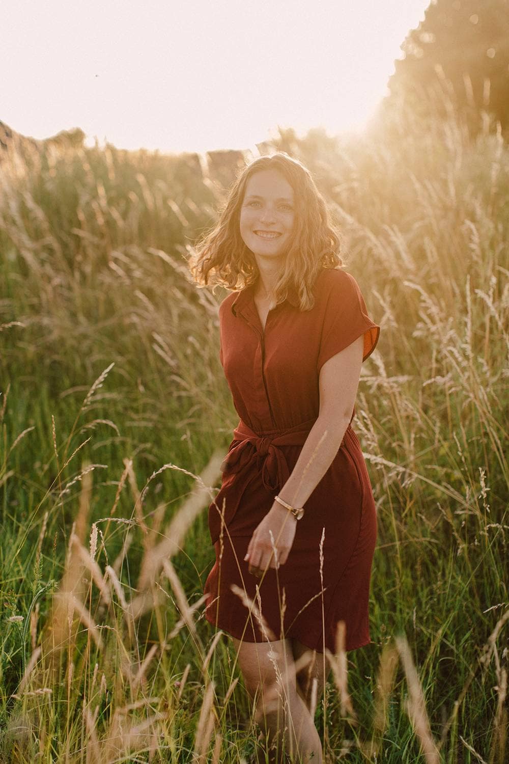 eine Frau steht in einem roten Kleid in einem Feld bei Sonnenuntergang